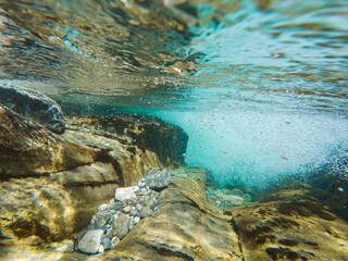 Crystal clear underwater shot of a fast-flowing Norwegian river, showing a rocky bed, sun rays, and thousands of oxygen bubbles.