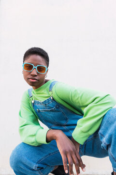 Young woman wearing sunglasses crouching in front of white wall