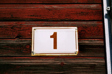Numéro 1. Plaque de numéro de rue sur façade en bois peint en rouge.