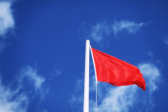Drapeau rouge &agrave; la plage. Baignade interdite. Drapeau flottant dans le vent sous fond de ciel bleu.