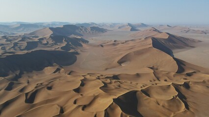 Aerial view of endless golden sand dunes ripple under the vast sky, casting long shadows across the arid landscape, Bam, Kerman Province, Iran.