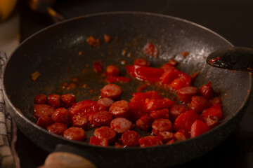 A skillet filled with flavorful sausages and ripe tomatoes, showcasing a vibrant meal preparation scene