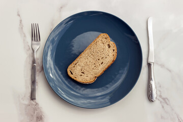 A conceptual image of a blue plate, fork and knife placed on a bright dining table. The concept: diet, food restriction, and mindful eating.
