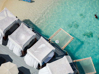 Aerial view of white cabanas lining the wooden pier against the turquoise sea, a scene of serene luxury and vibrant coastal contrast, Ksamil, Vlor, Albania.