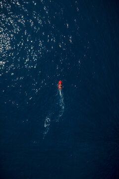 Aerial view of a solitary red boat cutting through the deep blue sea, creating a striking contrast in the vast expanse of the Ionian Sea, Ksamil, Vlor, Albania.
