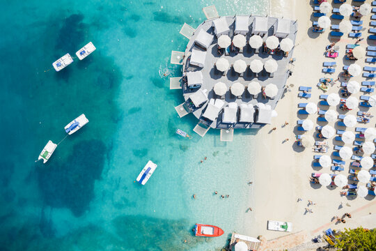 Aerial view of the vibrant beach, where turquoise waters meet the soft, sandy shore dotted with white umbrellas and boats, Ksamil, Vlor, Albania.