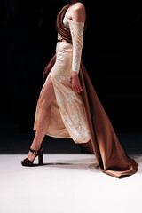 Fashion woman wearing yellow dress with silk brown cape, fancy cloth on black background. Fashion model walking the runway fashion show	