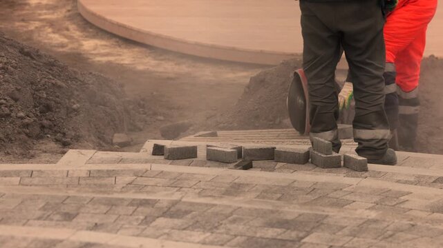 Close up of workers legs among bricks with cutting saw and working shoes at paving site