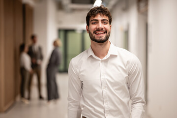 Obraz premium Smiling young businessman looking at camera in office corridor