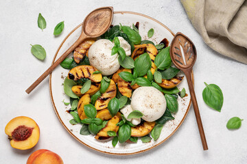 Mediterranean salad with burrata cheese, grilled peaches, fresh basil leaves, olive oil and balsamic glaze, gourmet summer dish on light background