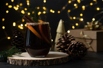 Festive winter mulled wine or punch with orange and cinnamon spices in a glass close-up view on dark  background of glowing holiday lights