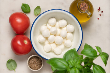 Marble light background with olive oil, basil, lemon, mozzarella and spices. Caprese salad ingredients  top view  for fresh Italian cooking concept