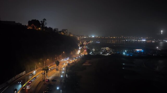 Aerial night view of Circuito de Playas highway in Lima, Peru. Illuminated traffic flowing along the dark coast of Pacific Ocean