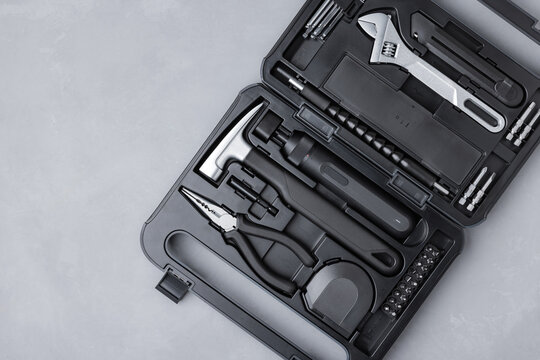 Toolbox with a variety of tools including a hammer, pliers, and a wrench on grey stone background, top view with copy space. The toolbox is open and the tools are visible.