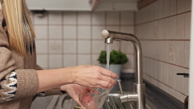 Woman washing glass jar under running water at kitchen sink, showcasing cleaning process with camera zooming in on action sequence