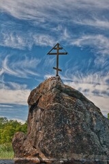 Large boulder in water with Orthodox wooden cross, northern Russia, summer, green trees in background, scenic and tranquil nature landscape