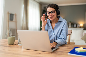 Fototapeta premium Happy freelance businesswoman in headphones leading remote coaching call from home workspace speaking to laptop during virtual webinar client consultation mentoring strategy planning home office