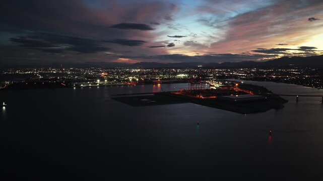 Cinematic drone shot of illuminated industrial shoreline at dusk, Mie, Japan