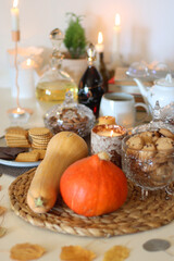 Lit candles, cookies, chocolate, nuts, tea, wine, pumpkins, books, reading glasses and autumn leaves on the table. Autumnal hygge at home. Selective focus.