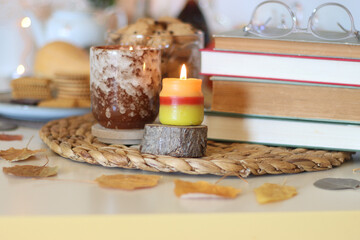 Lit candles, cookies, chocolate, nuts, tea, wine, pumpkins, books, reading glasses and autumn leaves on the table. Autumnal hygge at home. Selective focus.