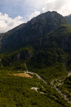 Aerial view of a dramatic landscape unfolds with rugged mountains rising above verdant forests and a winding river carving its path through the valley, Theth, Shkoder County, Albania.