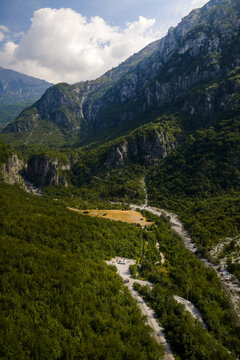 Aerial view of the rugged, verdant Albanian Alps cascade down to meet the winding river snaking through the valley, Theth, Shkoder County, Albania.