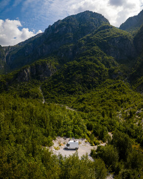 Aerial view of a lone campervan nestled in a gravel clearing, embraced by the verdant forest and towering mountains, Theth, Shkoder County, Albania.