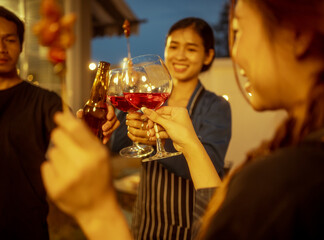 An Asian woman and friends toast with wine during a cozy backyard BBQ. Grilling skewers over charcoal under string lights, they celebrate friendship, joy,  togetherness in a festive outdoor evening