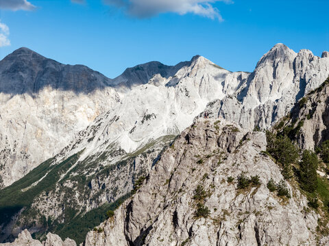 Aerial view of jagged, sun-drenched peaks and shadowy valleys carve a dramatic landscape under a clear blue sky, Teth, Shkoder County, Albania.
