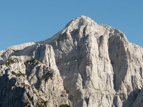 Aerial view of a stark, rocky mountain peak piercing a clear blue sky, its rugged texture contrasting with the smooth expanse above, Teth, Shkoder County, Albania.