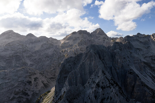 Aerial view of rugged, grey mountain peaks rise sharply against a bright sky dotted with fluffy white clouds, Teth, Shkoder County, Albania.