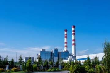 Obraz premium Modern power plant with two red and white striped chimneys on a clear sky. Industrial facility for energy generation.