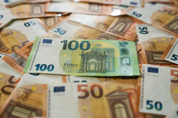 Close up of European Euro Banknotes Stacked with a bright green One Hundred note on top of Multiple Fifty Cash Currency Background