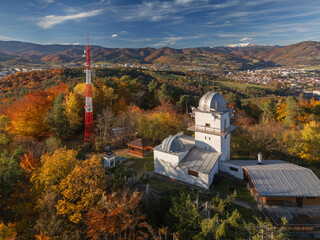Aerial view of the Vartovka astronomical observatory amidst vibrant autumn foliage, with a striking red and white tower piercing the skyline, Banska Bystrica, Banskobystricka kraj, Slovakia.