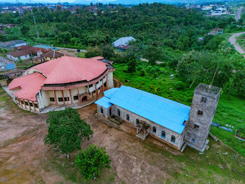 Aerial view of the striking contrast between the red-roofed circular building and the blue-roofed rectangular structure amidst the lush greenery, Ede, Osun, Nigeria.