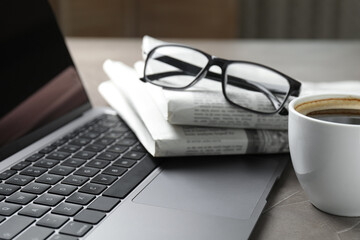 Newspapers, laptop, coffee and glasses on grey table, closeup