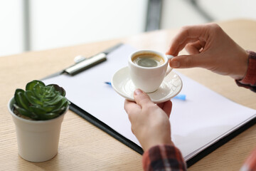 Woman having coffee break at wooden desk indoors, closeup