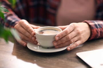 Coffee break. Woman with cup of aromatic drink at wooden desk indoors, closeup