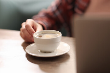 Coffee break. Woman with cup of aromatic drink at wooden desk indoors, closeup