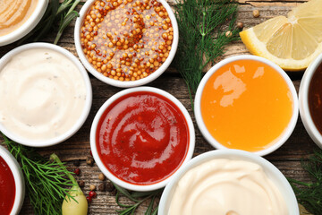 Different sauces in bowls and ingredients on wooden table, flat lay