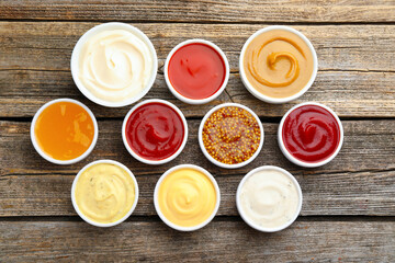 Different sauces in bowls on wooden table, flat lay