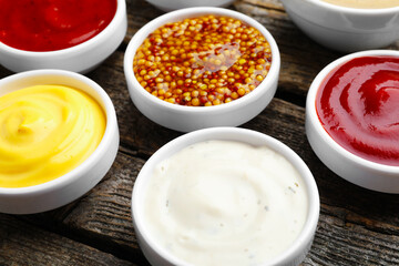 Different sauces in bowls on wooden table, closeup