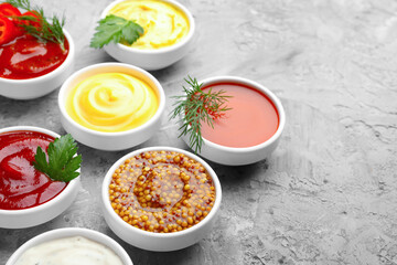 Different sauces in bowls and ingredients on grey textured table, closeup. Space for text