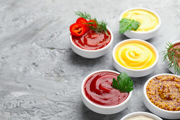 Different sauces in bowls and ingredients on grey textured table, closeup. Space for text