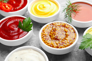 Different sauces in bowls and ingredients on grey textured table, closeup