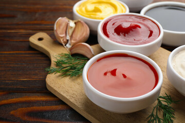 Different sauces in bowls and ingredients on wooden table, closeup