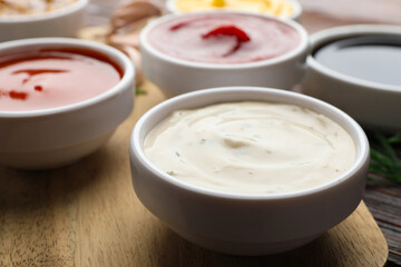 Different sauces in bowls on wooden table, closeup