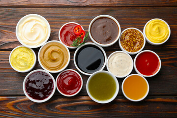 Different sauces in bowls on wooden table, flat lay