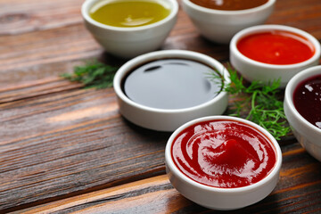 Different sauces in bowls with fresh dill on wooden table, closeup. Space for text