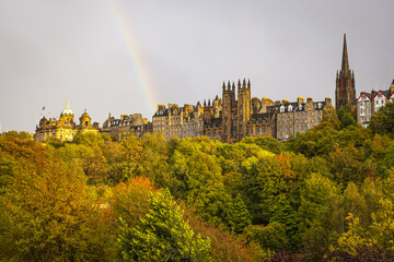 View of a vibrant rainbow arches over a historic skyline amidst a tapestry of autumnal foliage, casting a golden glow on ancient architecture, Edimburg, Scotland, United Kingdom.